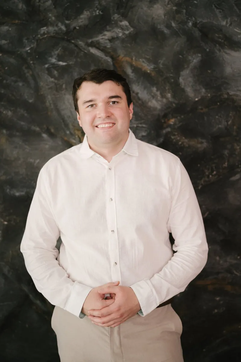 Jakob Sebov, Inhaber von Jakse Apartments, lächelnd vor einer dunklen Steinwand